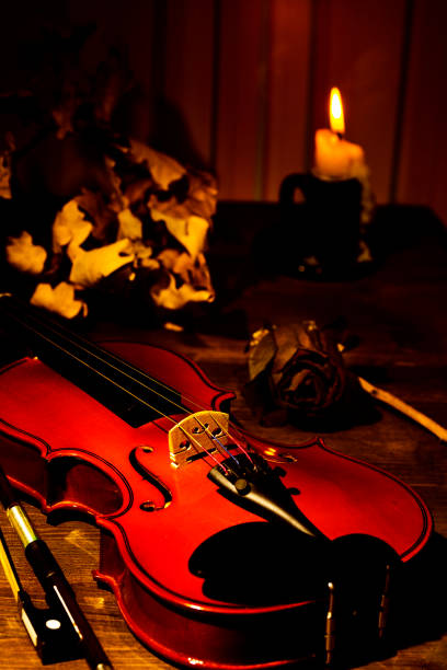 Violin and autumn leaves on the on the table in light of candle in the dark room. Close-up of violin. Focus on the strings.