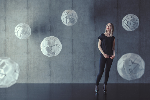 Young woman with abstract glass sphere against concrete background.