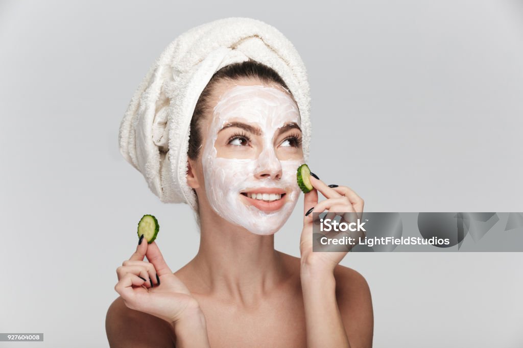白で隔離顔スキンケア マスクとキュウリのスライスを持つ若い女性 - フェイスパックのロイヤリティフリーストックフォト