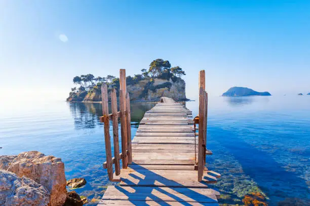 Greece. Picturesque wooden pedestrian Bridge to the small atoll island, view from great Greek Zante or Zakinthos island. Beautiful morning scenery in sunny spring day.