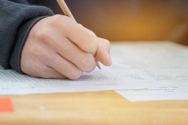 istock high school or university student hands taking exams, writing examination on paper answer sheet optical form of standardized test on desk doing final exam in classroom. Education  literacy concept. 927611604