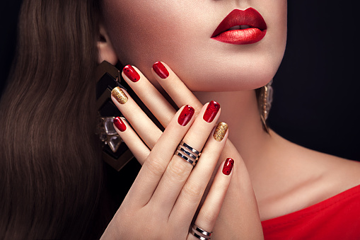 Beautiful woman with perfect make-up and red and golden manicure wearing jewellery on black background