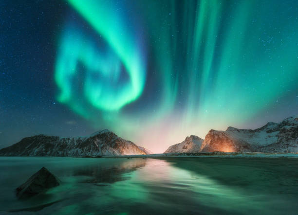 aurora borealis in lofoten islands, norway. aurora. green northern lights. starry sky with polar lights. night winter landscape with aurora, sea with sky reflection, stones, beach and snowy mountains - norway island nordic countries horizontal imagens e fotografias de stock