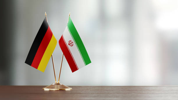 German And Iranian Flag Pair On A Desk Over Defocused Background