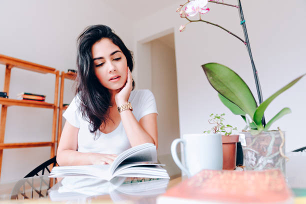 istock Young woman reading a book at home 927632896