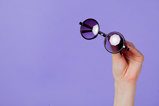 Female hand holding round sunglasses on purple background