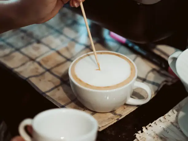Photo of Barista drawing Latte art on the coffee with a small stick.