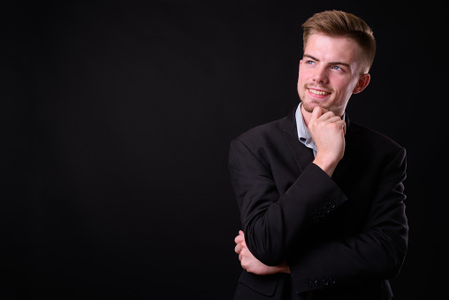 Studio shot of young handsome bearded businessman with blond hair against black background