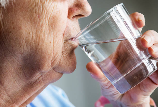 vista laterale dell'acqua potabile della donna anziana - usare la bocca foto e immagini stock