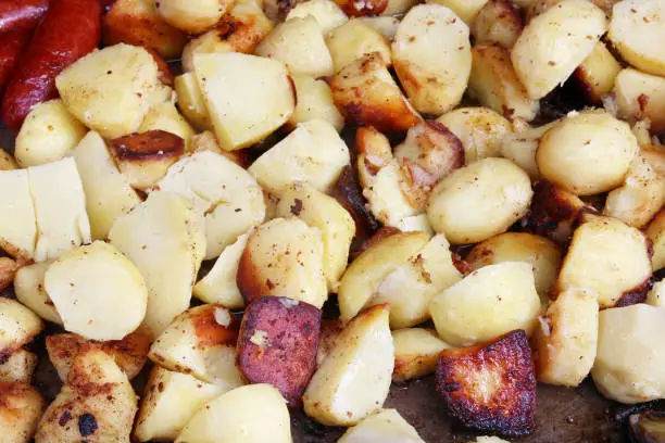Fast street-food - smoked pork sausages and fried potato  in big iron black frying pan. Spring fair day closeup shot