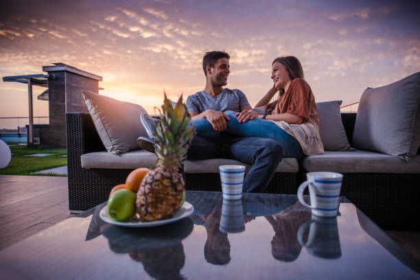istock Happy couple talking to each other while relaxing on sofa at penthouse patio. 927740880