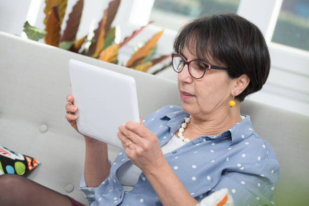 istock mature brunette woman sitting on the sofa using digital tablet 927743992