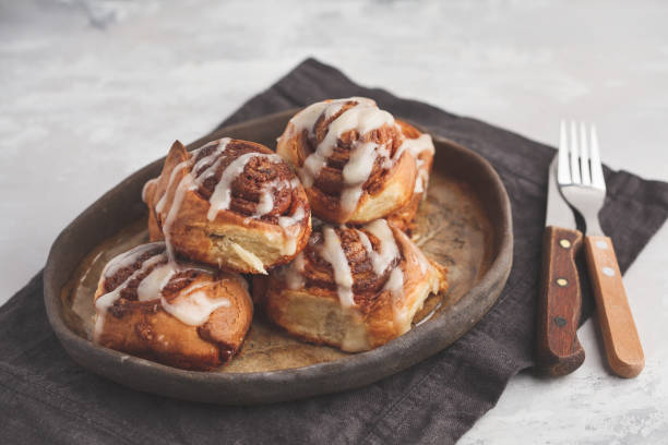 istock Homemade cinnamon buns in glaze on a dark dish, light background, copy space, top view. 927745254