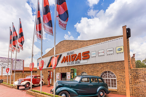 Spare parts store shop front Midas with two vintage vehicles parked outside the front door, in Mpumalanga, South Africa.