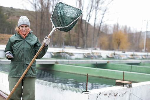 Portrait of young female worker of fish farm standing with landing net outdoors