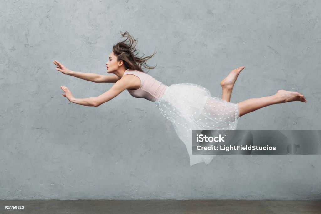 beautiful young woman in dress levitating and looking away on grey Women Stock Photo