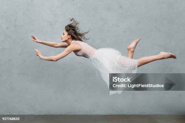 Beautiful Young Woman In Dress Levitating And Looking Away On Grey Stock Photo - Download Image Now