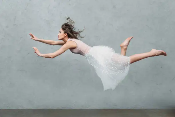 Photo of beautiful young woman in dress levitating and looking away on grey