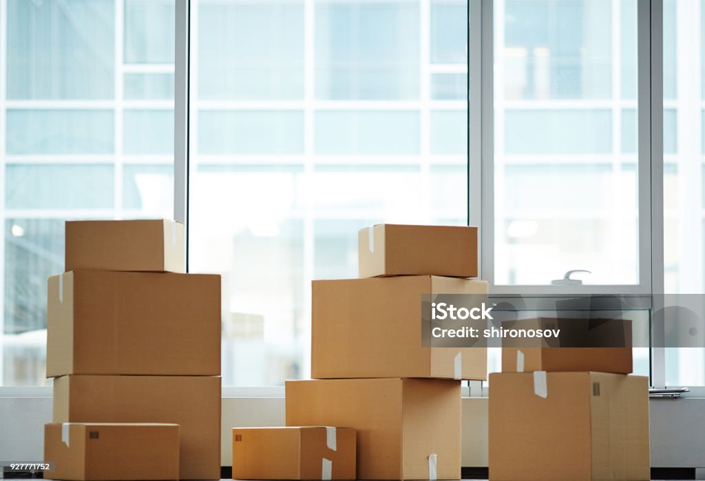 Packed boxes Row of three stacks of packed boxes by window of new office just after relocation Office Stock Photo