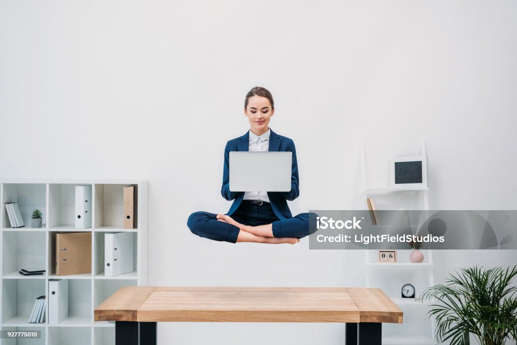 souriante jeune femme d’affaires avec ordinateur portable tout en lévitation au bureau - Photo de Lévitation libre de droits