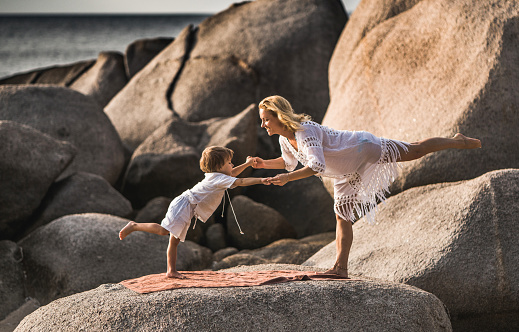Happy mother and son cooperating while exercising balance on a rock at the beach.