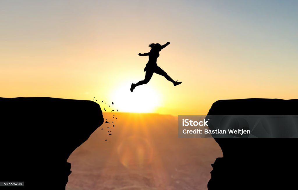 Woman jumping over abyss. Woman jumping over abyss in fornt of sunset. Courage Stock Photo
