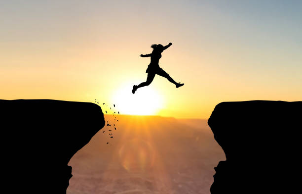 Woman jumping over abyss. Woman jumping over abyss in fornt of sunset. ravine stock pictures, royalty-free photos & images