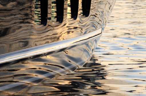 Large super yacht hull reflecting the water with ripples and the soft light of the sunset.