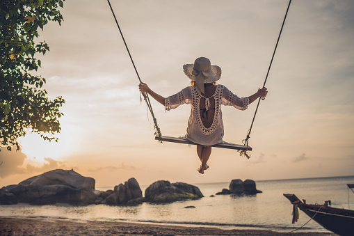 Rear view of a woman swinging during summer vacation on a beach.
