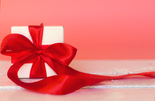 white  small gift box with thin red ribbon on white wood table with pink background