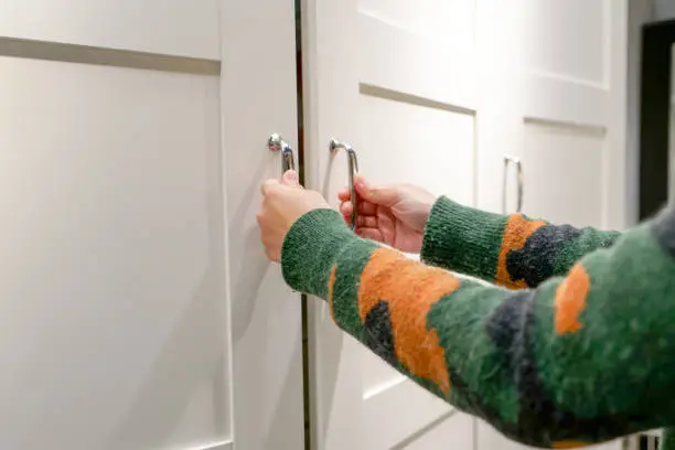 Photo of women hands open the cupboard/cabinet door, white wooden door