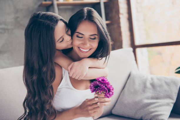 koncepcja dnia kobiet! zdumiona radosna urocza mama trzyma ładne kwiaty i otrzymuje pocałunek od swojej małej uroczej córki z długimi kręconymi włosami - flower spring bouquet child zdjęcia i obrazy z banku zdjęć