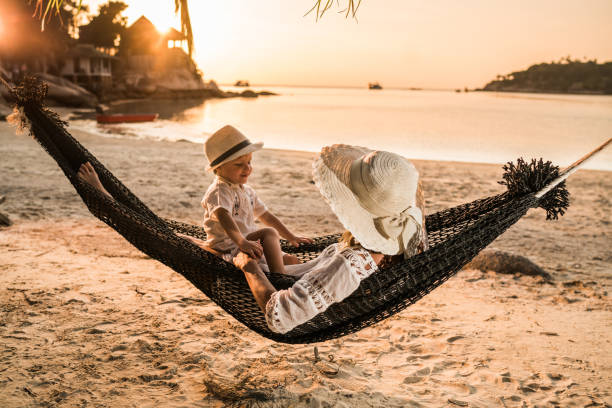 un ragazzino che parla con sua madre su un'amaca da spiaggia al tramonto. - hammock beach vacations tropical climate foto e immagini stock