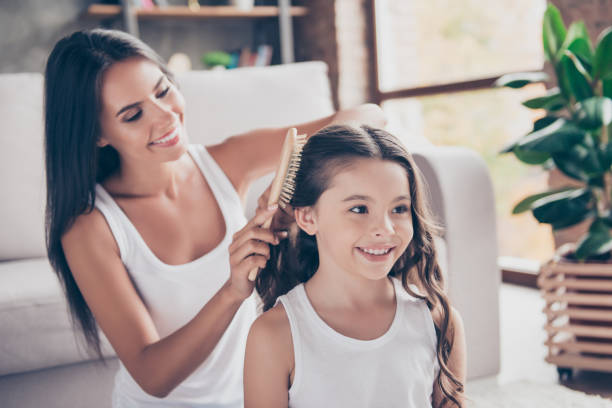 Close up photo of happy smiling schoolgirl with curly long dark hair and her beautiful mum who is brushing her hair, they are dressed in white tshirts Close up photo of happy smiling schoolgirl with curly long dark hair and her beautiful mum who is brushing her hair, they are dressed in white tshirts brushing photos stock pictures, royalty-free photos & images