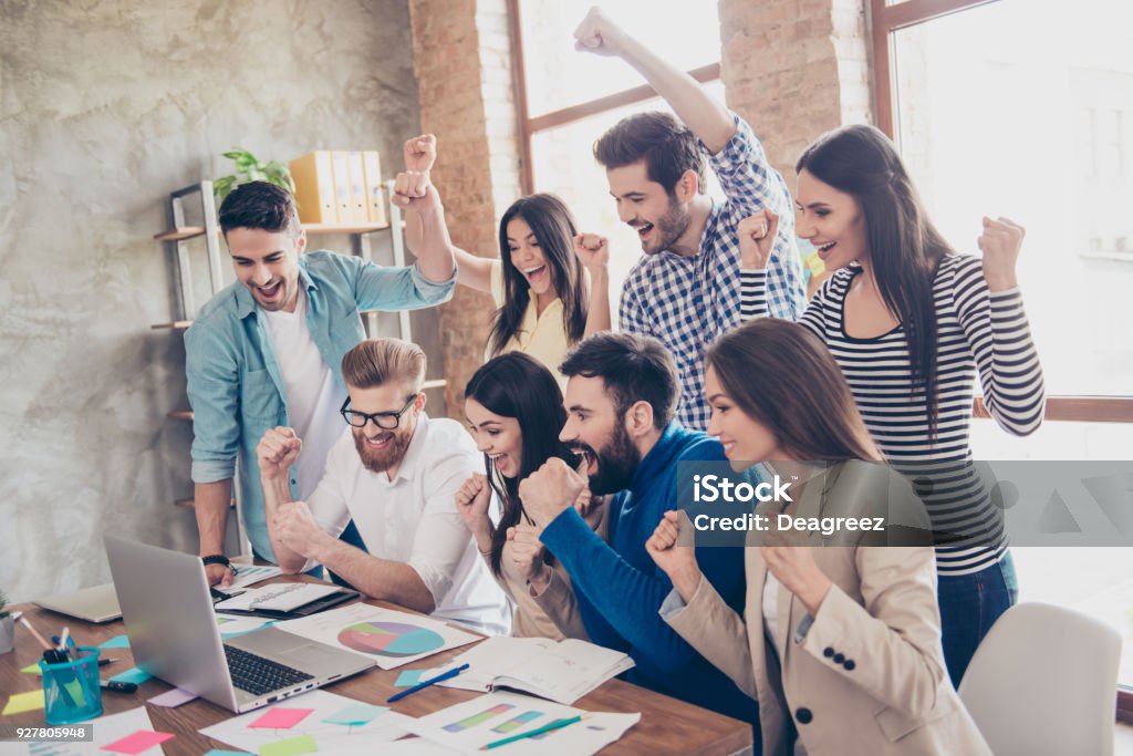 Success and team work concept. Group of business partners with raised up hands in light modern workstation, celebrating the breakthrough in their company Teamwork Stock Photo