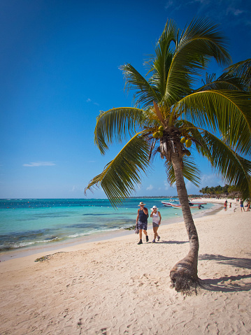 A beautiful Caribbean beach on the Yucatan peninsular in Mexico near Tulum with a couple in swimwear walking along the water's edge.