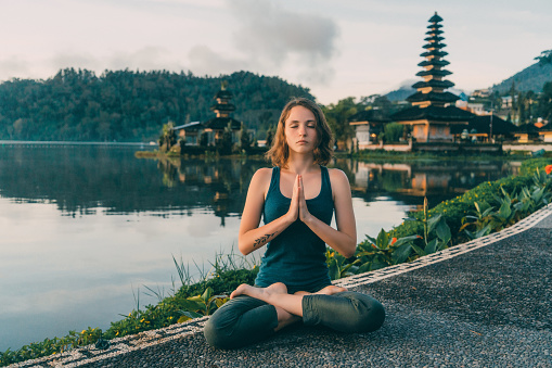 Young Caucasian woman  doing yoga near  Ulun Danu Temple  in  Bali  at sunrise