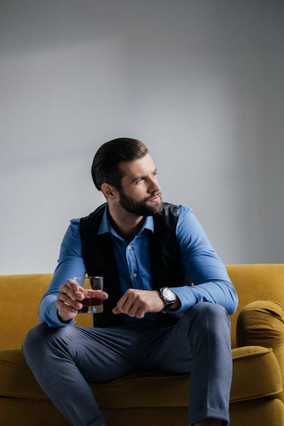 istock stylish man holding alcohol drink and sitting on yellow sofa 927817352