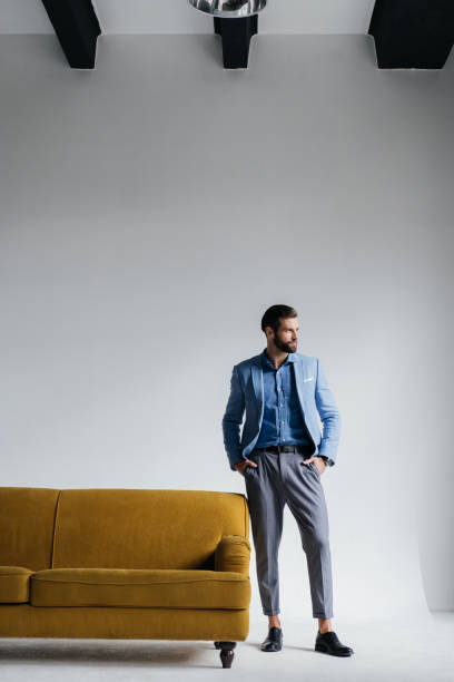 istock stylish man in blue suit posing at yellow couch 927817564