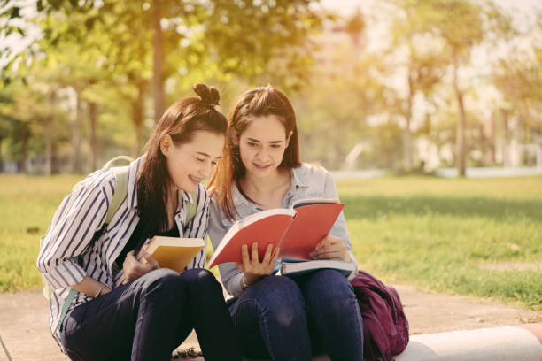 istock Young women together study reading book in university and knowledge at outside or park campus relaxing smile in summer season 927826520
