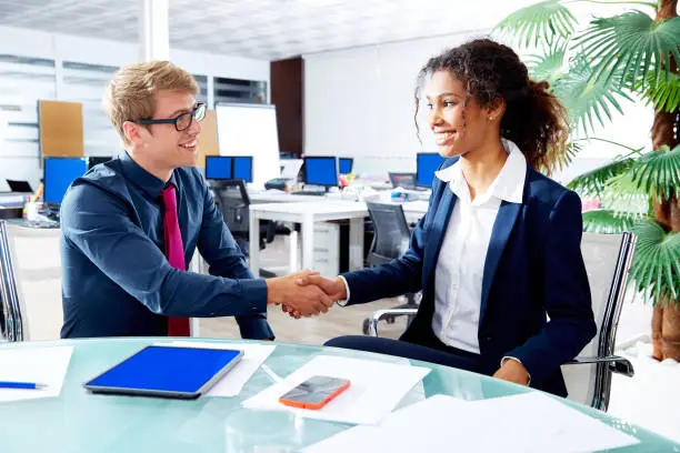 Executive handshake blond businessman and african businesswoman in office meeting