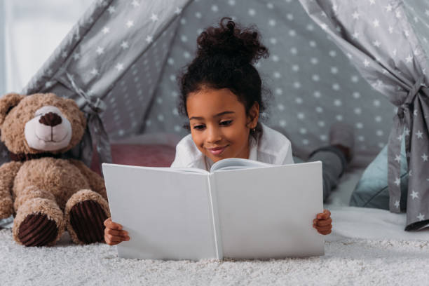 adorable african american kid reading book and lying in tent at home adorable african american kid reading book and lying in tent at home teddy bear photos stock pictures, royalty-free photos & images