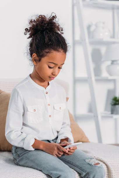 istock adorable african american kid using smartphone on sofa 927837882