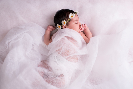 2 weeks newborn baby girl sleeping on a wool fabric, wearing chamomile flower headband.