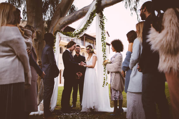 Young couple getting married with bride giving groom wedding ring at ceremony with multi-ethnic friends