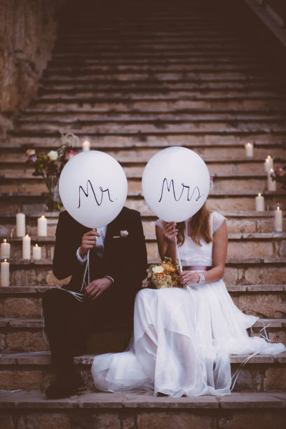 istock Bride and groom sitting on stone steps and holding balloons 927856646