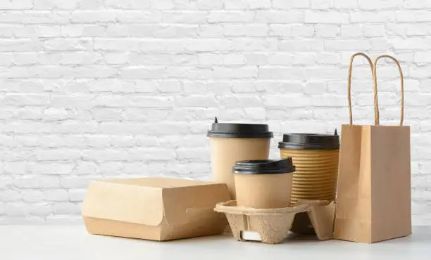 Fast food packaging set. Paper coffee cups in holder, food box, brown paper bag on the table