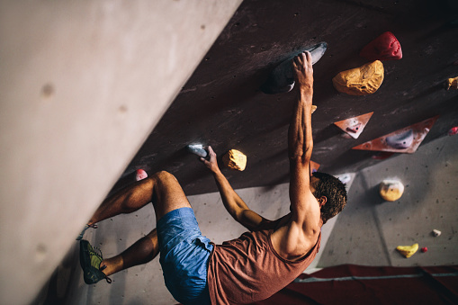 Athletic man bouldering at an indoor climbing centre. Professional climber climbing wall upside down at an indoor climbing gym.