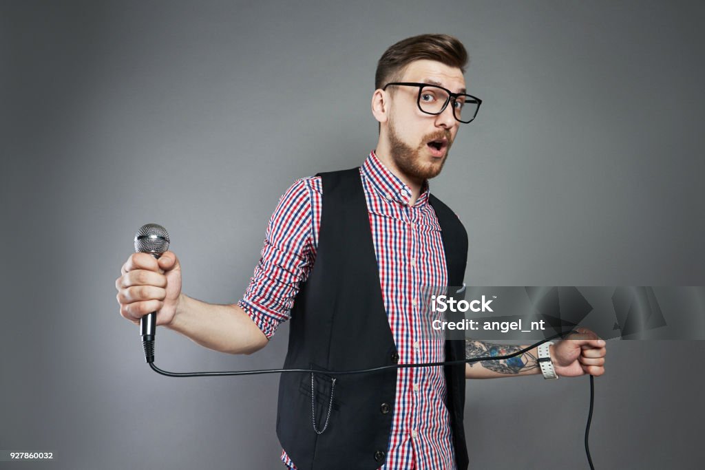 Karaoke Man Sings The Song To Microphone Singer With Beard On Grey Background  Funny Man In Glasses Holding A Microphone In His Hand At The Karaoke Singer  Sings The Song Stock Photo -