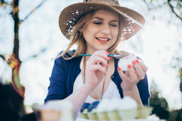 istock Smiling young woman decorating Easter eggs outdoors on a sunny day 927860512